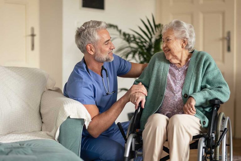A caregiver in uniform assists an older adult with organizing daily pill containers at a small table.